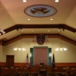 Courtroom interior with judge's bench, American flag, wooden furnishings, and ornate ceiling details.